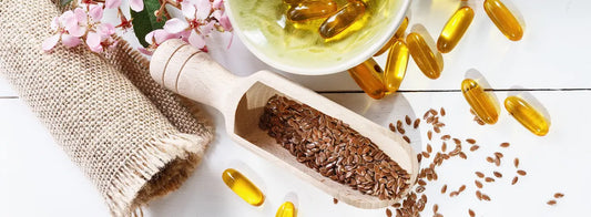 Flaxseeds, golden flaxseed oil and a clear supplement capsule arranged on a clean background.